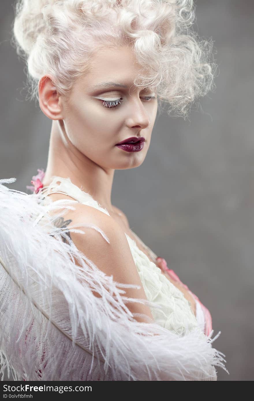 Young attractive woman with platinum blonde and purple lipstick. Fantasy style portrait of a lady with white curls and white feather.