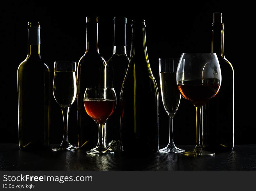 Bottles of wine and different glasses of wine on a dark background