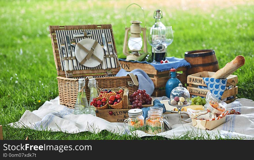 Vintage style picnic hamper with lunch in a park spread out on a rug on the grass with cheese, fresh fruit, bonbons, pickles bread and red wine. Vintage style picnic hamper with lunch in a park spread out on a rug on the grass with cheese, fresh fruit, bonbons, pickles bread and red wine