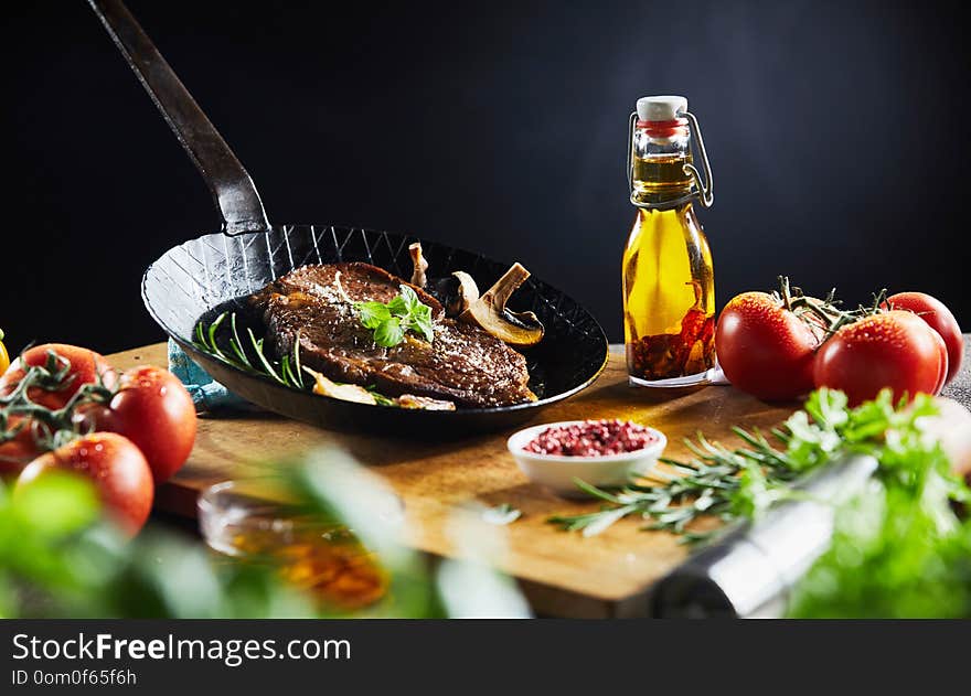 Prepared grilled steak with herbs and fresh mushrooms in a skillet surrounded by fresh ingredients and olive oil in a close up view. Prepared grilled steak with herbs and fresh mushrooms in a skillet surrounded by fresh ingredients and olive oil in a close up view