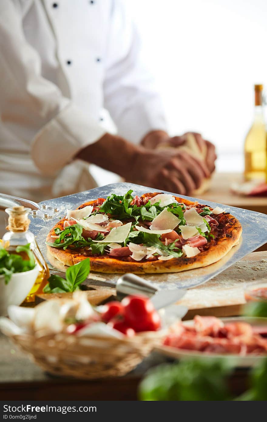 Chef seasoning a pizza topped with rocket cheese and tomato in a pizzeria in a close up on his hands. Chef seasoning a pizza topped with rocket cheese and tomato in a pizzeria in a close up on his hands