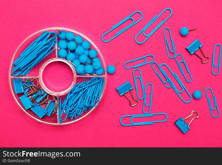 Stationery paper clips, binders and buttons in blue on pink background. Stationery paper clips, binders and buttons in blue on pink background