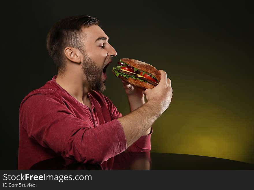 Young man eating tasty burger on color background.