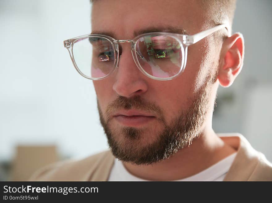 Young man wearing glasses on blurred background, closeup. Ophthalmology service