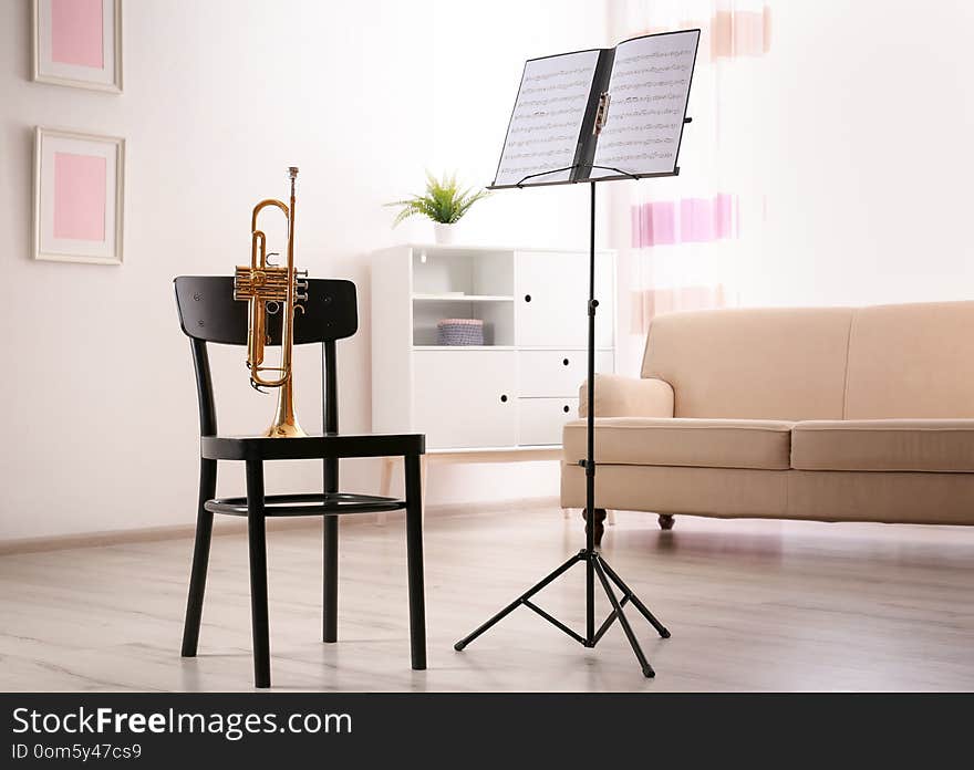 Trumpet, chair and note stand with music sheets in room