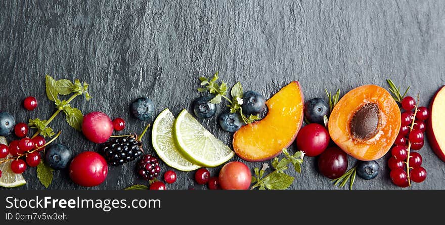 Banner concept with fresh fruit pieces and berries on dark grey stone background with wide copy space. Banner concept with fresh fruit pieces and berries on dark grey stone background with wide copy space