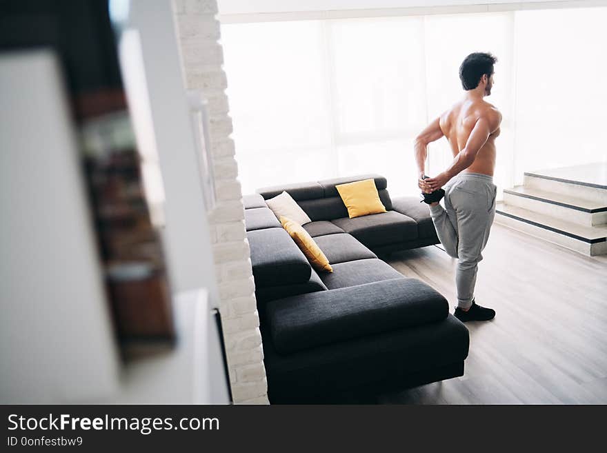 Bare chested young man stretching muscles before starting a workout routine. Handsome hispanic male athlete exercising for wellness in his living room. Latino people doing fitness and sport at home. Bare chested young man stretching muscles before starting a workout routine. Handsome hispanic male athlete exercising for wellness in his living room. Latino people doing fitness and sport at home.