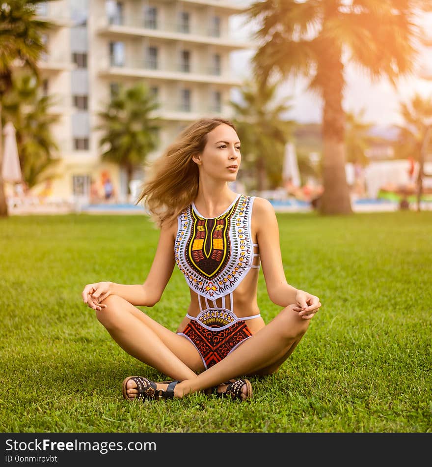 Young beautiful girl wearing fashion swimsuit monokini with a national african ethnic pattern sitting on a lawn