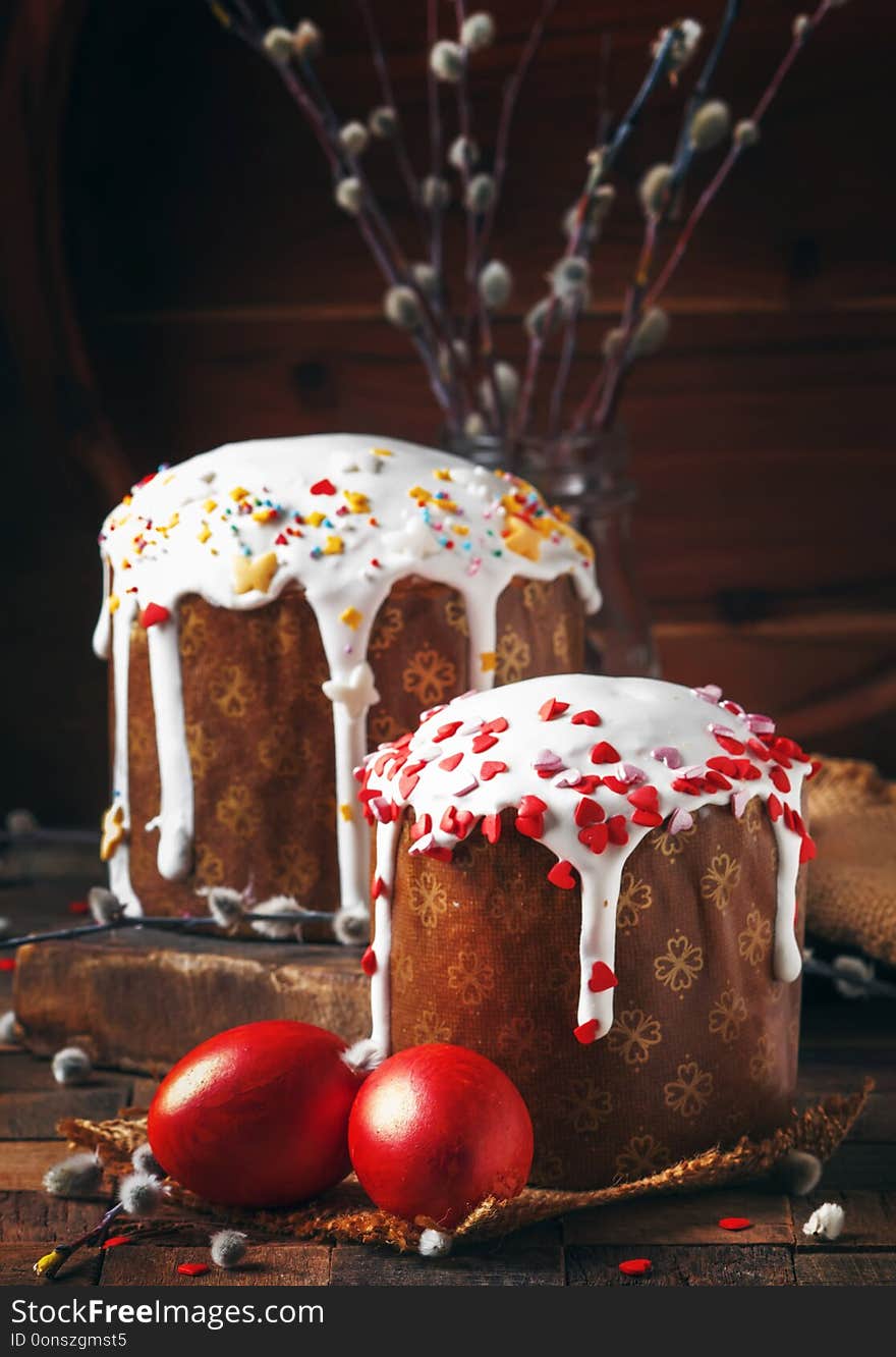 Happy Easter! Traditional Russian easter cake Kulich with colored red eggs, decorated with hearts, with twigs of fluffy willow. Vintage wooden table background, rustic style. Selective focus