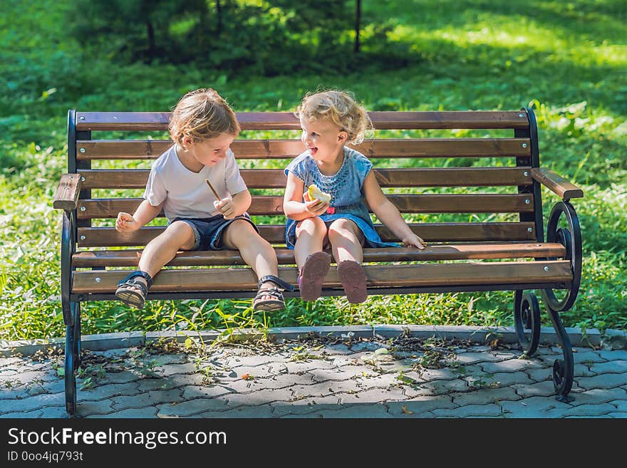 Toddlers boy and girl sitting on a bench by the sea and eat an apple.