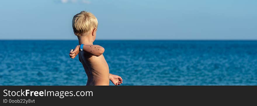 Blonde toddler boy throwing stone into a sea