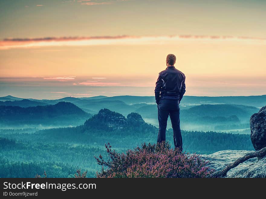 Man tourist traveler standing on cliff of mountain and looking to sunset, against backdrop of hills. Concept active recreation in mountains