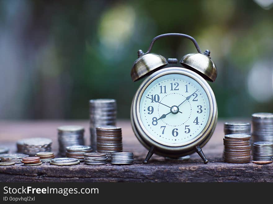 Vintage alarm clock and coin stacks on wooden table with blur green garden background, bright morning color tone, finance and