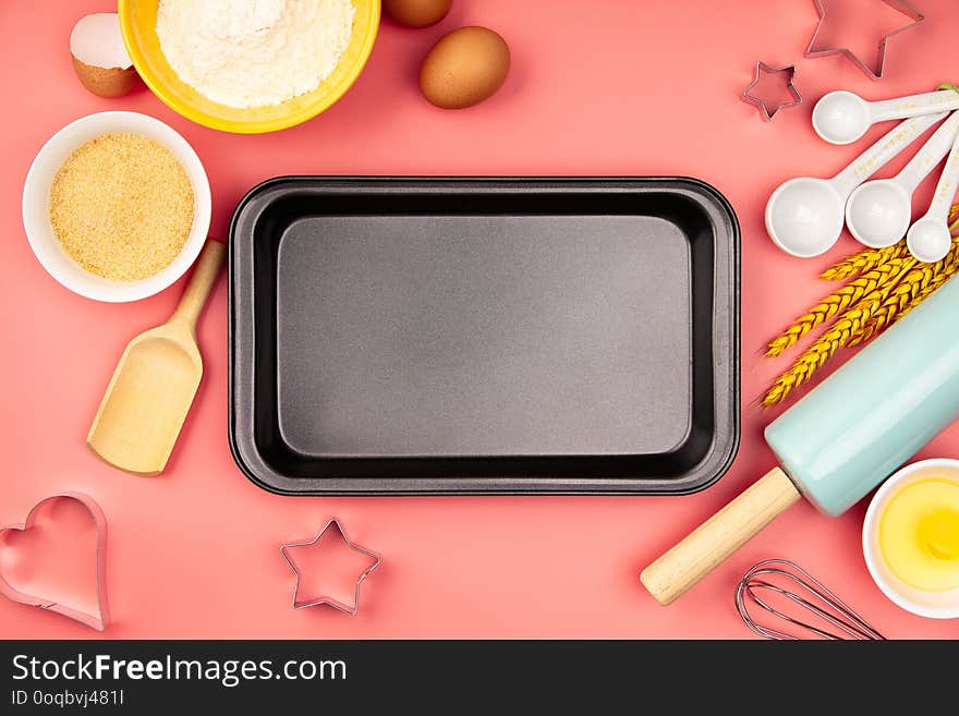 Baking ingredients and empty baking tray on pink background, flat lay. Ingredients, kitchen items for baking. Kitchen utensils, flour, eggs, sugar. Text space, top view