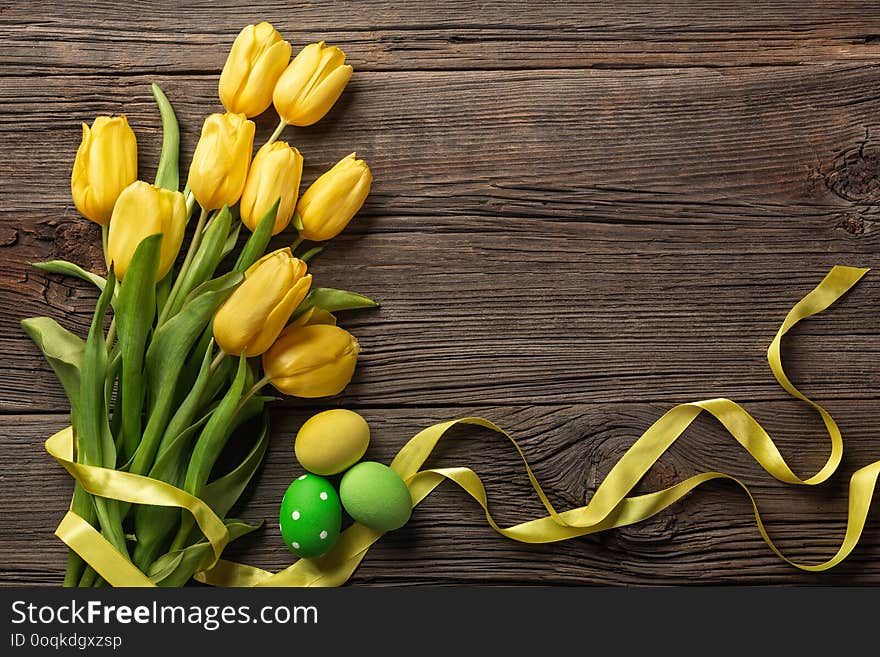 Yellow tulips in a paper bag, a nest with Easter eggs on a wooden background. Top view with copy space