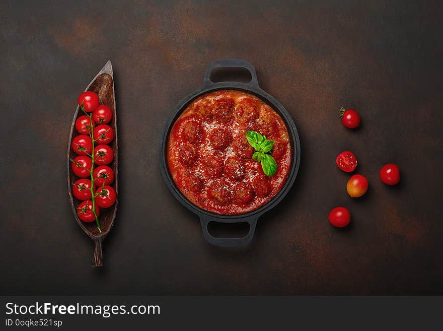 Meatballs in tomato sauce with spices, cherry tomatoes, pasta and basil in a frying pan on rusty brown background