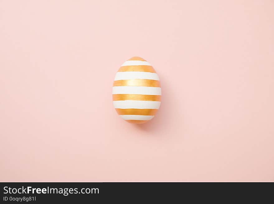 Easter golden with striped patternd egg on pastel pink background. Minimal easter concept. Happy Easter card with copy space for text. Top view, flatlay. Concept for banner, flyer, invitation, greeting card, holiday backgrounds.