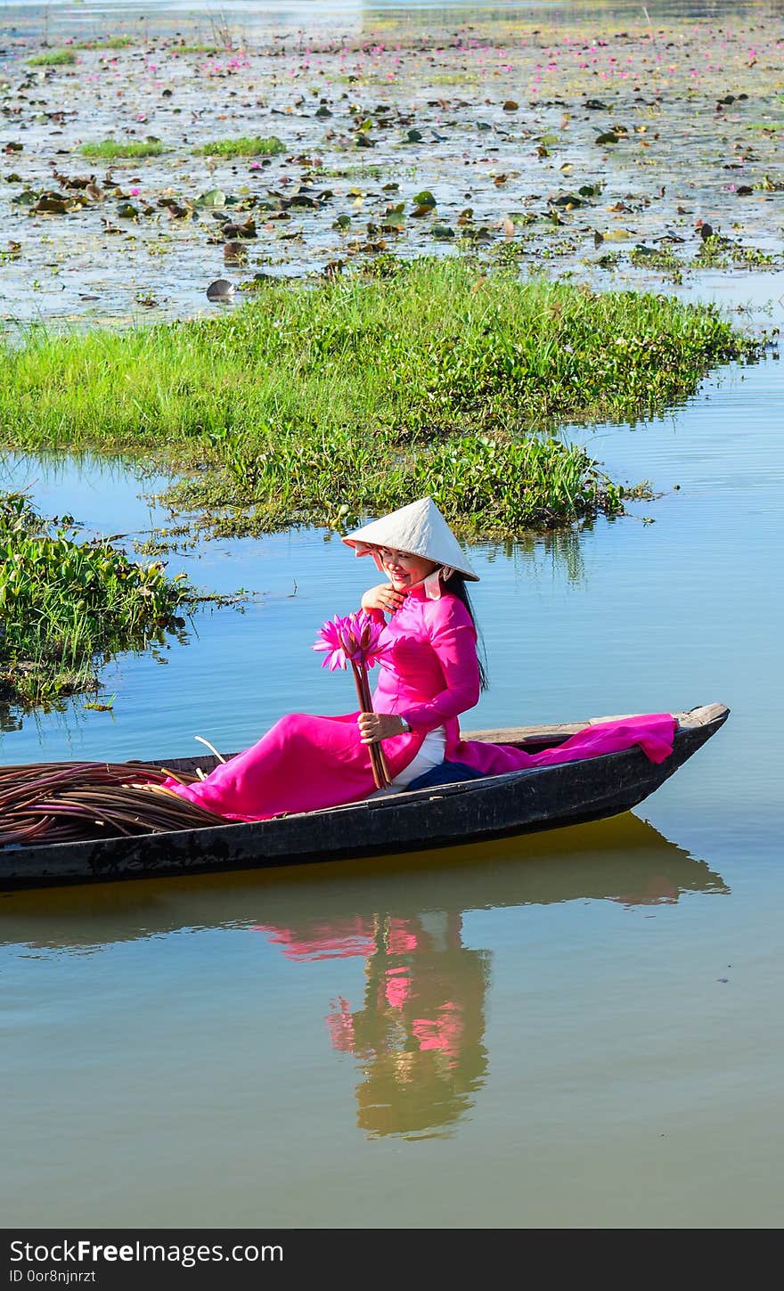 Asian woman in traditional dress Ao Dai sitting on the wooden boat in waterlily pond. Asian woman in traditional dress Ao Dai sitting on the wooden boat in waterlily pond