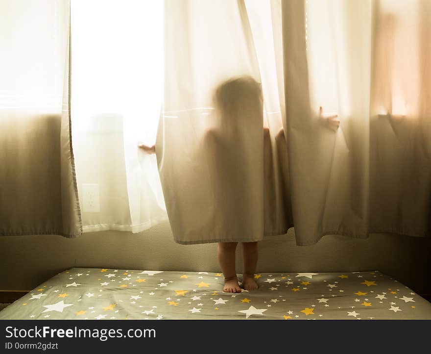 Toddler portrait of a young caucasian boy playing in the window curtains. Toddler portrait of a young caucasian boy playing in the window curtains.