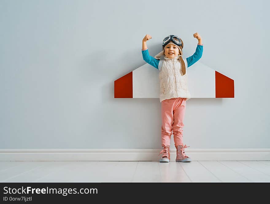 Little child girl in an astronaut costume is playing and dreaming of becoming a spaceman. Portrait of funny kid on a background of grey wall