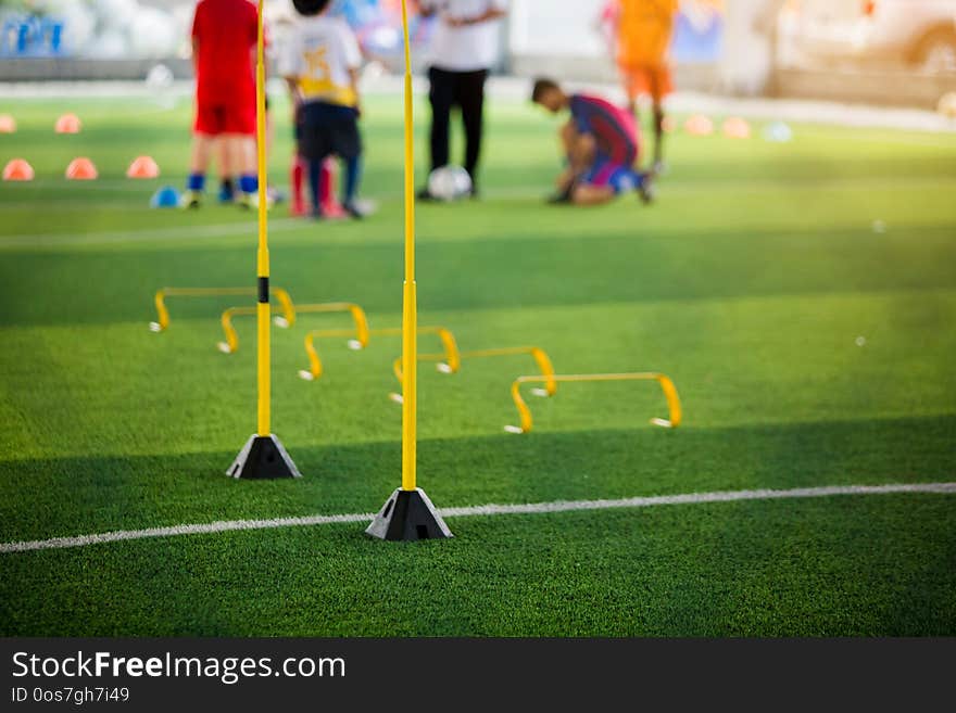 Yellow hurdles and ladder drills on green artificial turf with blurry coach and kid soccer are training