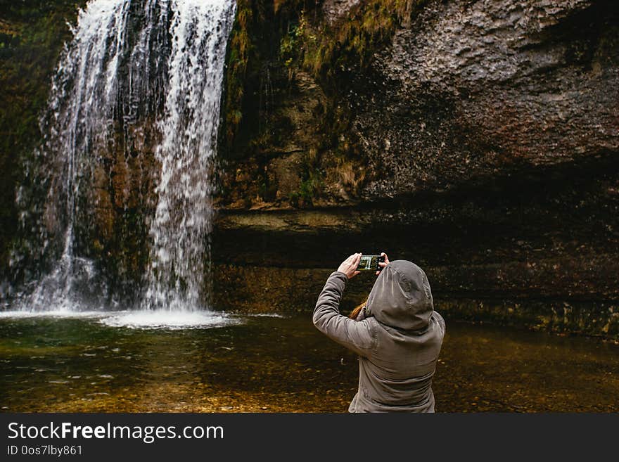 Woman taking a picture of a waterfall in a forest. Cascades du Hérisson, France.