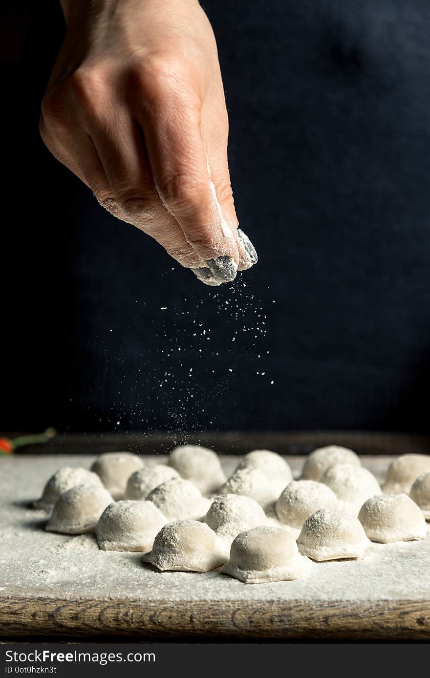 Uzbek national food Chuchvara, like dumplings, lie in the shape of a heart, on a wooden board, hands are crushing flour from above