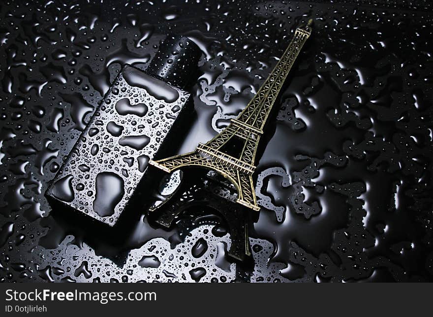 Bottle of French men&#x27;s perfume, statuette of the Eyfeleve tower with water drops on a black background. Fashion concept