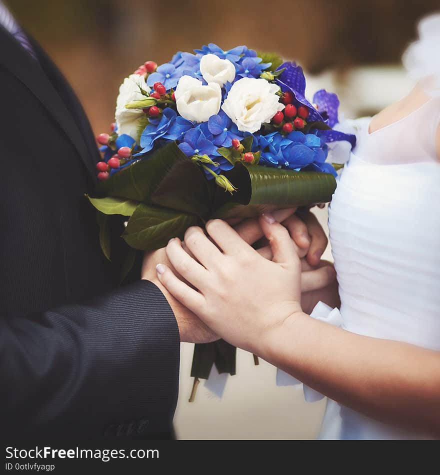 The bride and groom hold a beautiful wedding bouquet of flowers between each other. The bride and groom hold a beautiful wedding bouquet of flowers between each other.