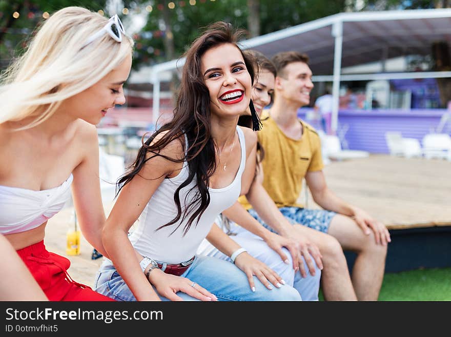 A company of good-looking friends laughing and socialising while sitting on the bench in the nice summer cafe. Cheers. Entertainment, having good time. Friendship. .