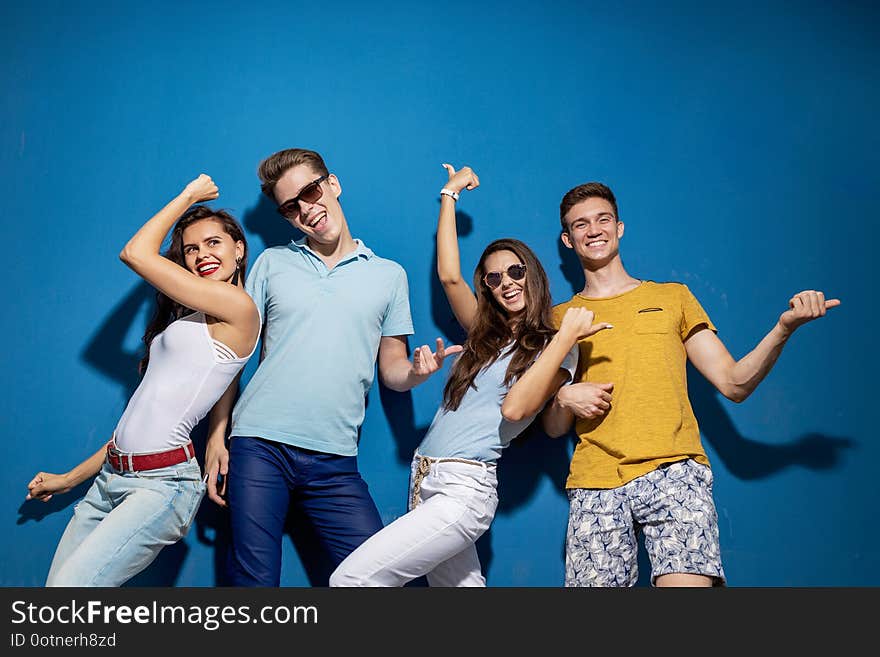 Four good-looking friends are laughing while standing in front of the blue wall having confident and happy looks. Entertainment, having good . Friendship, relationship. .
