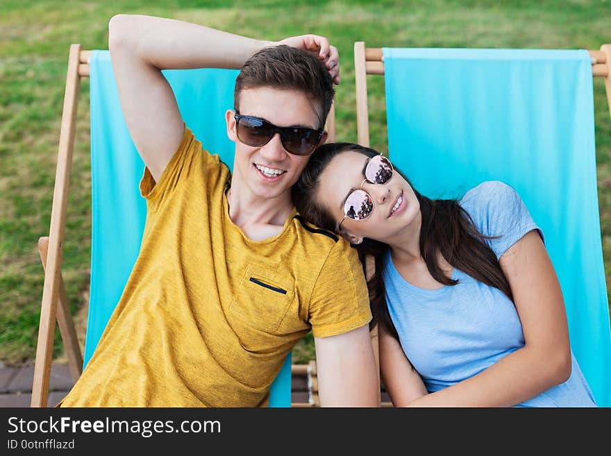 A beautiful couple in the sunglasses is lying on the deck chairs on the lawn in the nice summer cafe. Entertainment, having good . Friendship, relationship. .