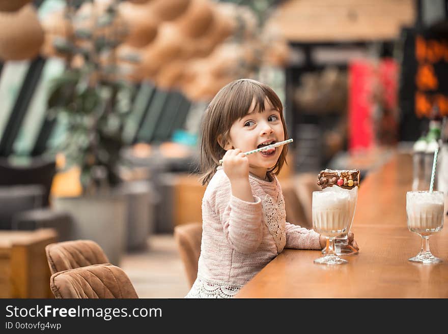 Charming Funny little girl drinks a milkshake in a restaurant, licking a tube. Baby food fast food . Leisure in the cafe