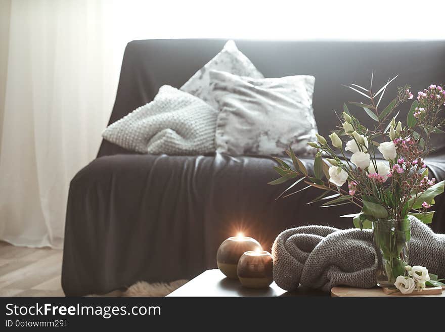 Cozy home interior with elements of decor in the living room with a black sofa and a vase of flowers and lighted candles on a small table. Cozy home interior with elements of decor in the living room with a black sofa and a vase of flowers and lighted candles on a small table