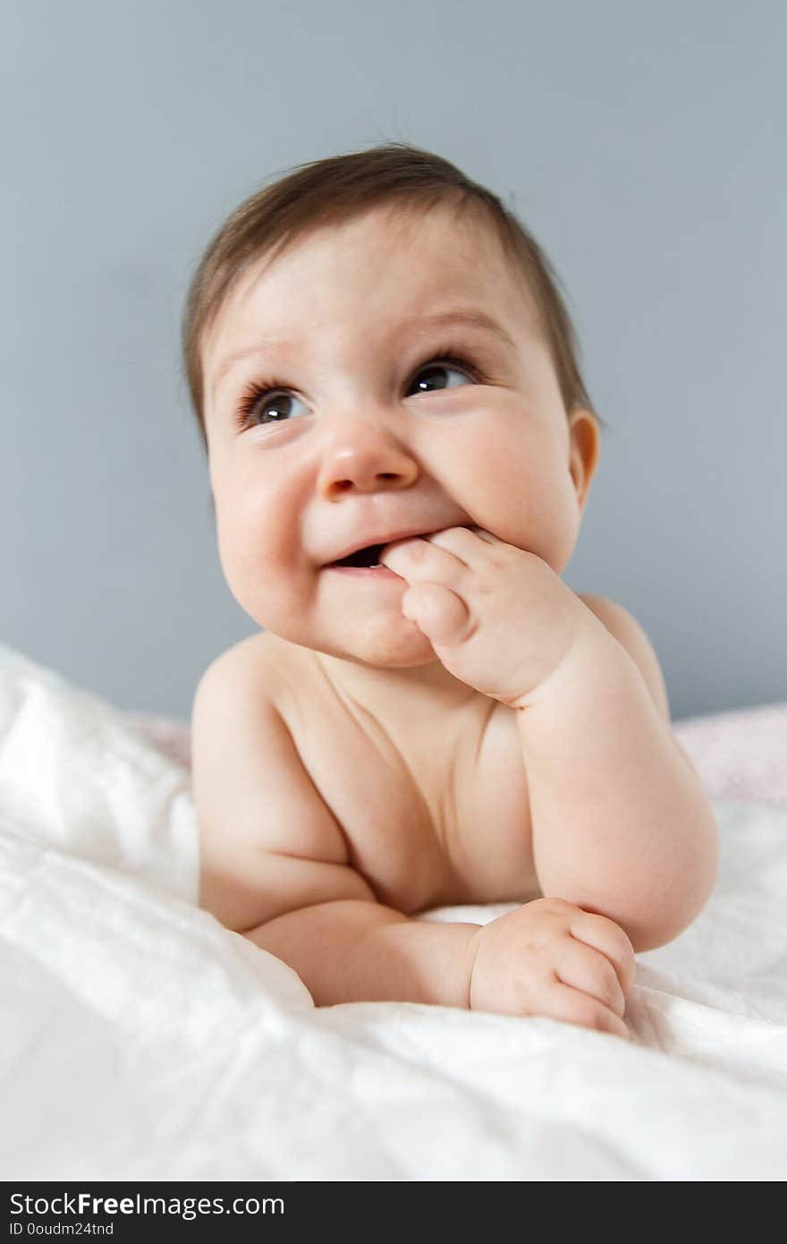 Portrait of beautiful baby lying on stomach and looking straight. Infant is. Isolated on grey background.