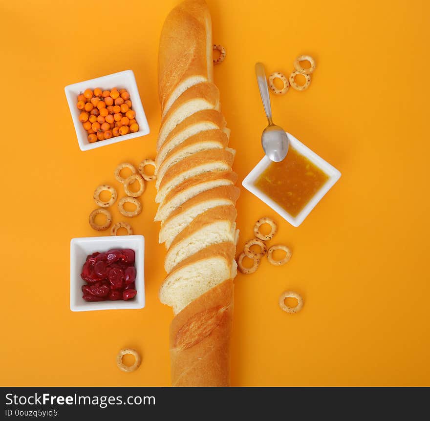 Top view of sliced french bread, jam, cottage cheese and butter on orange background. Appetizing still life of baking and jam. Top view of sliced french bread, jam, cottage cheese and butter on orange background. Appetizing still life of baking and jam