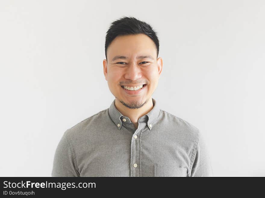 Happy and laughing face of ordinary Asian man in grey shirt. Concept of charming laugh