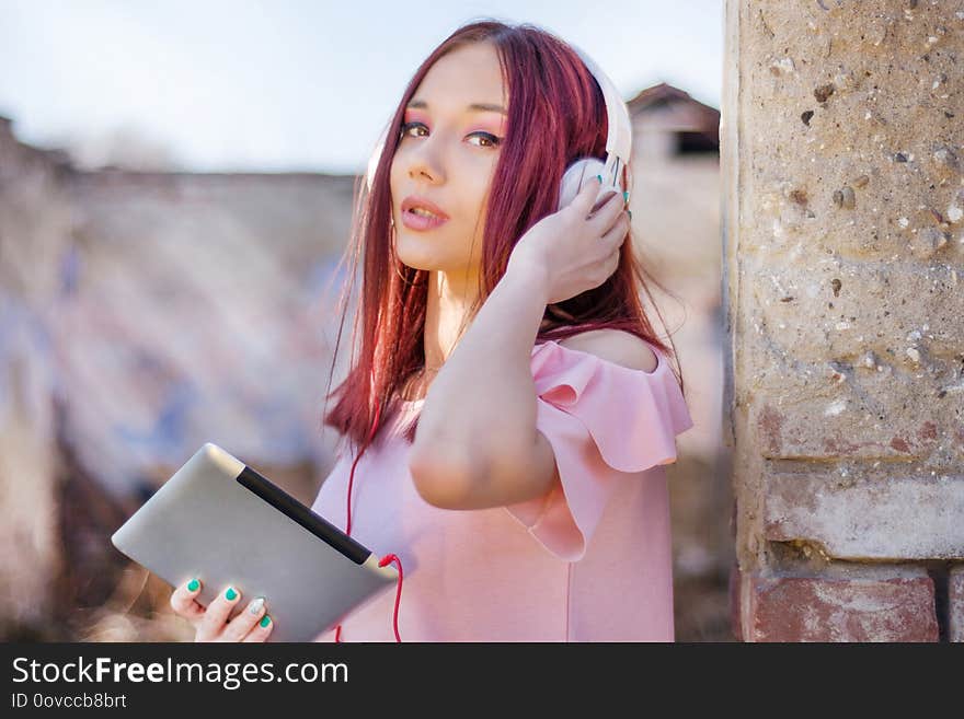 Redhead woman with headphones using tablet and listening to music on old ruins building