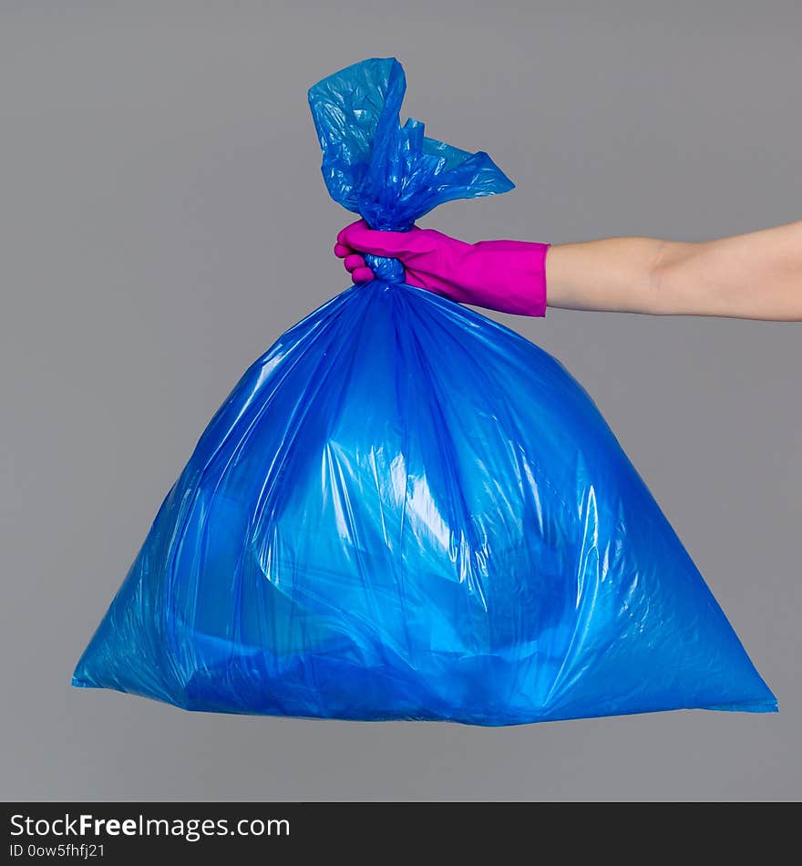 A woman`s hand in a rubber glove holds a blue plastic bag full of garbage