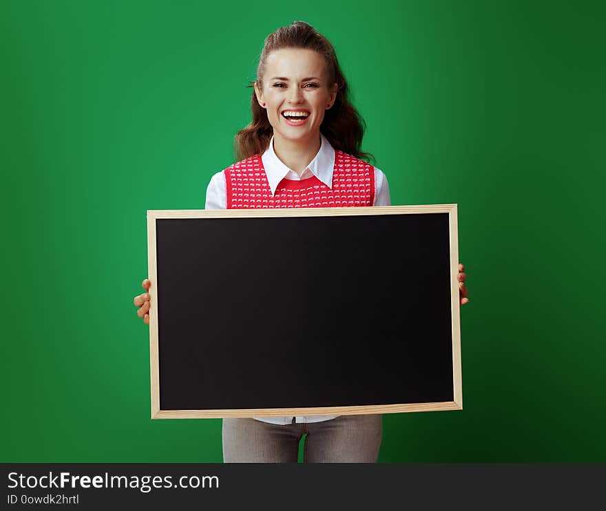 Smiling young student woman in grey jeans and pink sleeveless shirt showing blackboard isolated on chalkboard green. Smiling young student woman in grey jeans and pink sleeveless shirt showing blackboard isolated on chalkboard green