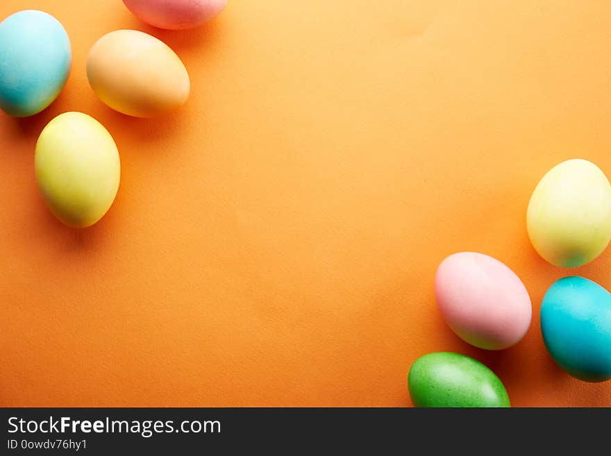 Bunch of blank painted Easter eggs of different pastel color on bright orange paper background with a lot of copy space for text. Top view, flat lay, close up. Easter greeting card concept. Bunch of blank painted Easter eggs of different pastel color on bright orange paper background with a lot of copy space for text. Top view, flat lay, close up. Easter greeting card concept