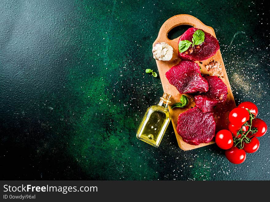 Raw beef meat steaks, with olive oil and spices, dark green concrete background copy space top view