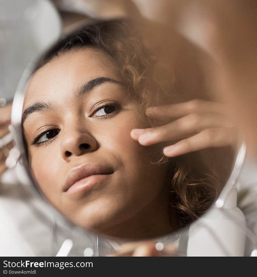 Afro-american girl looking herself in round mirror in bathroom. Perfect skin care concept