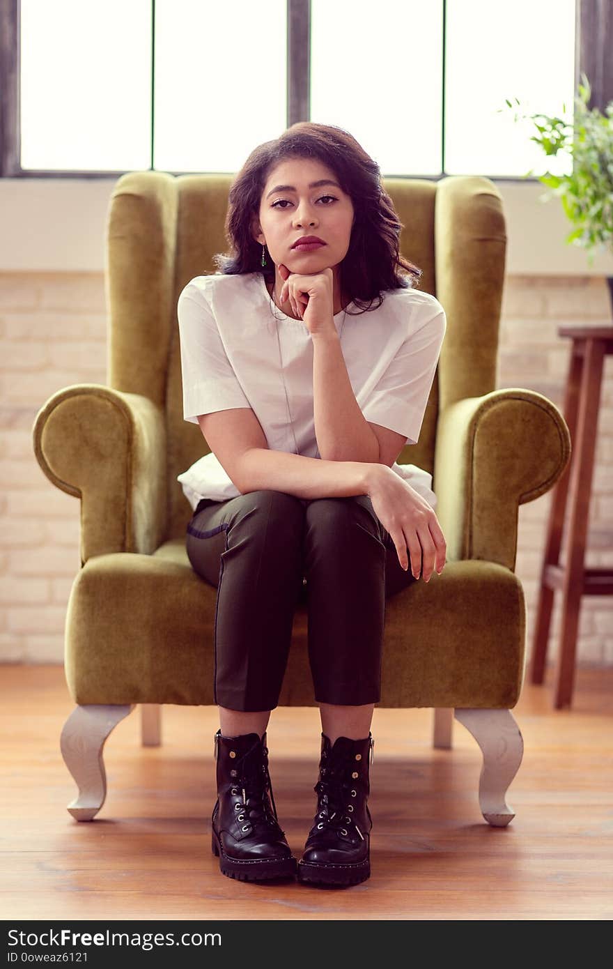 Serious look. Beautiful dark haired woman looking at you while sitting in the armchair