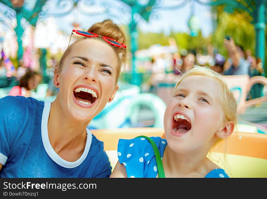 Smiling modern mother and child travellers in amusement park enjoying ride