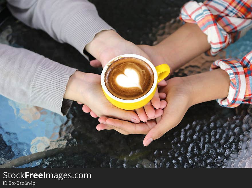 Romantic couple in love hand holding two cups of latte art with pattern the heart on table in coffee shop