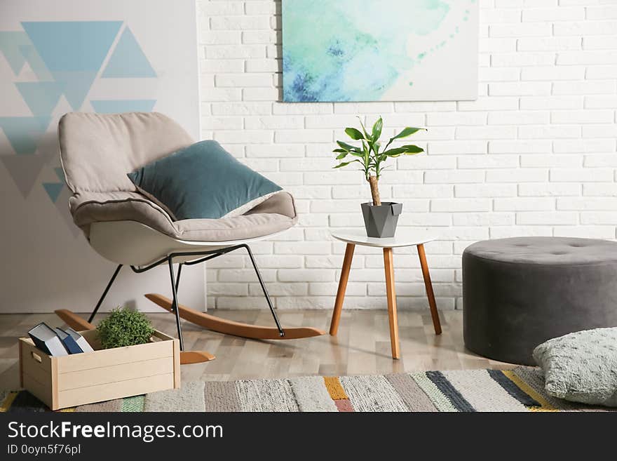 Comfortable rocking chair near brick wall in modern room interior