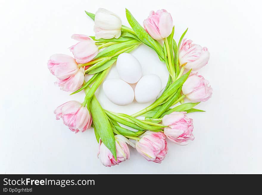 Easter eggs in nest and pink fresh tulip bouquet on rustic white wooden background