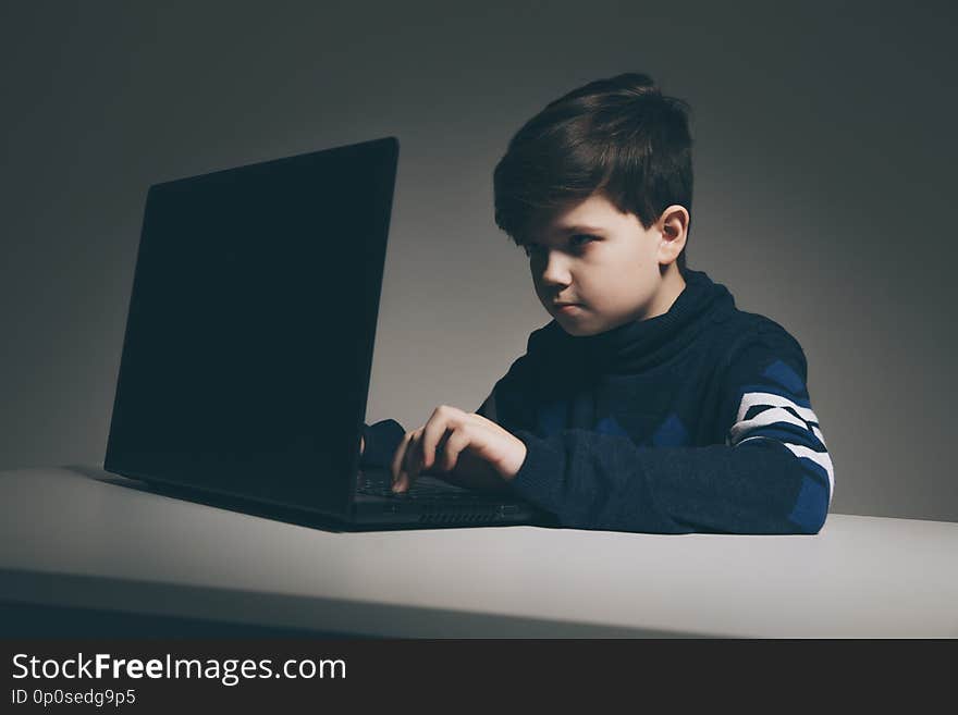 Photo of nice boy in sweater sitting infront of the computer doing homework.