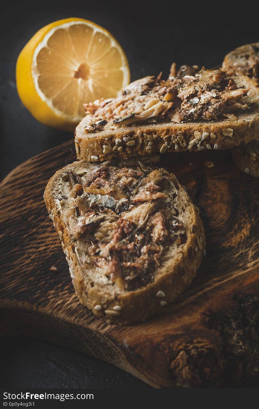 Slices of multigrain bread with sprats. Dark light.